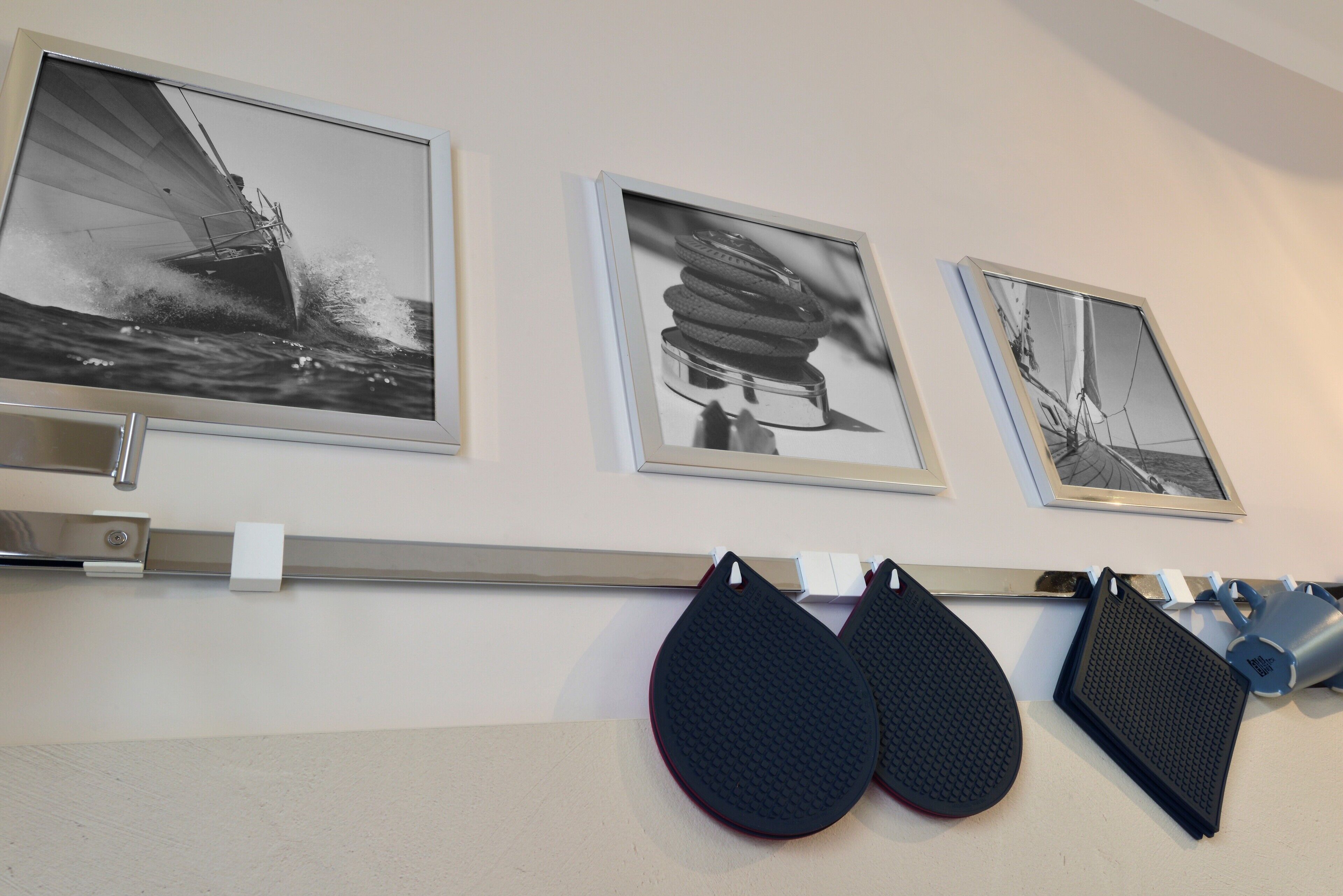 Framed black and white photographs on a wall, a metal shelf with a white object, and two black, textured objects hanging below.