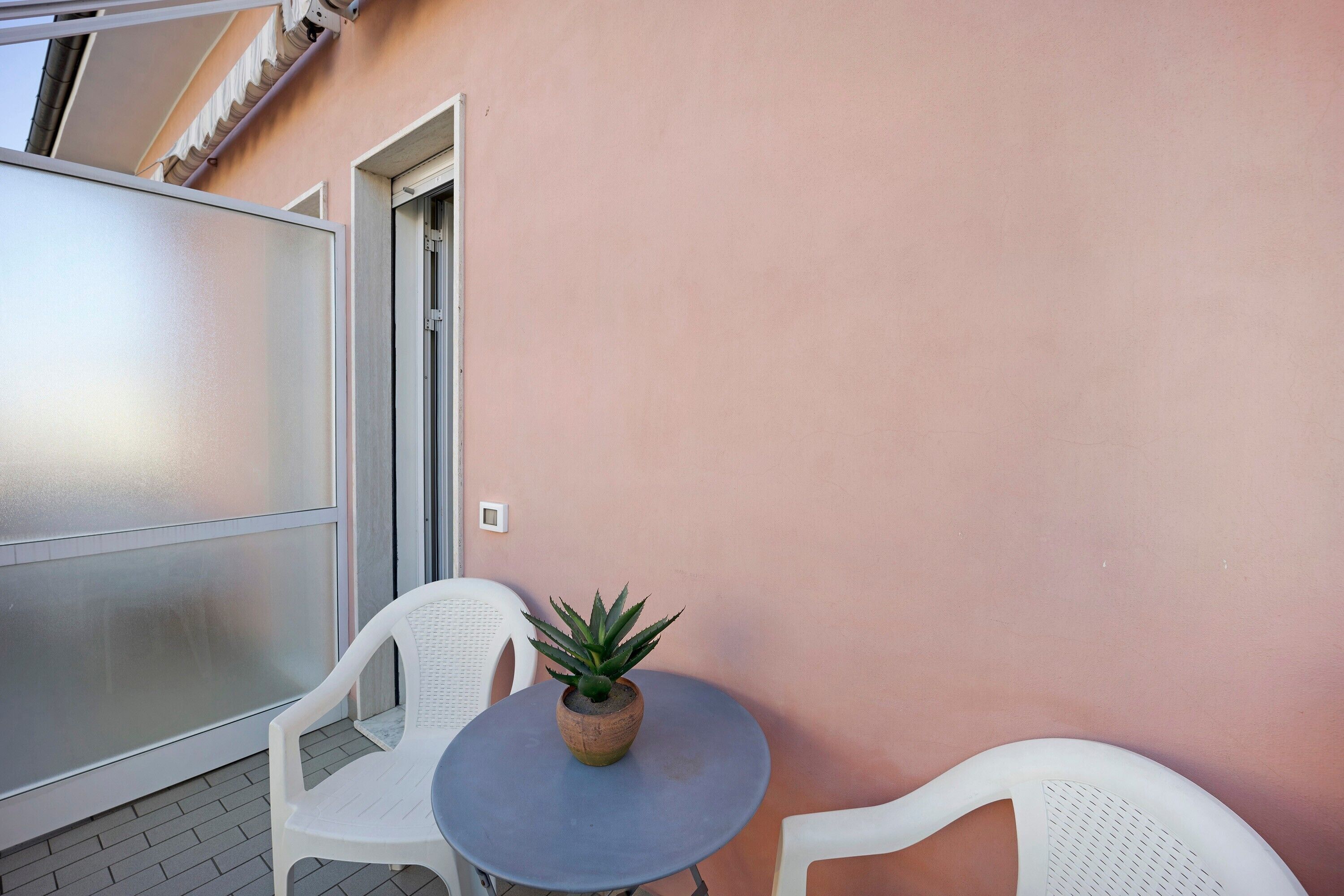 Un balcon avec une table ronde, deux chaises blanches et une plante en pot.
