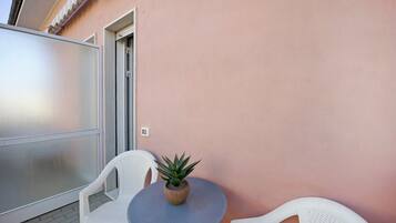 Un balcon avec une table ronde, deux chaises blanches et une plante en pot.