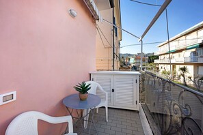 Un balcon avec une chaise blanche, une petite table ronde ornée d’une plante et un meuble blanc.