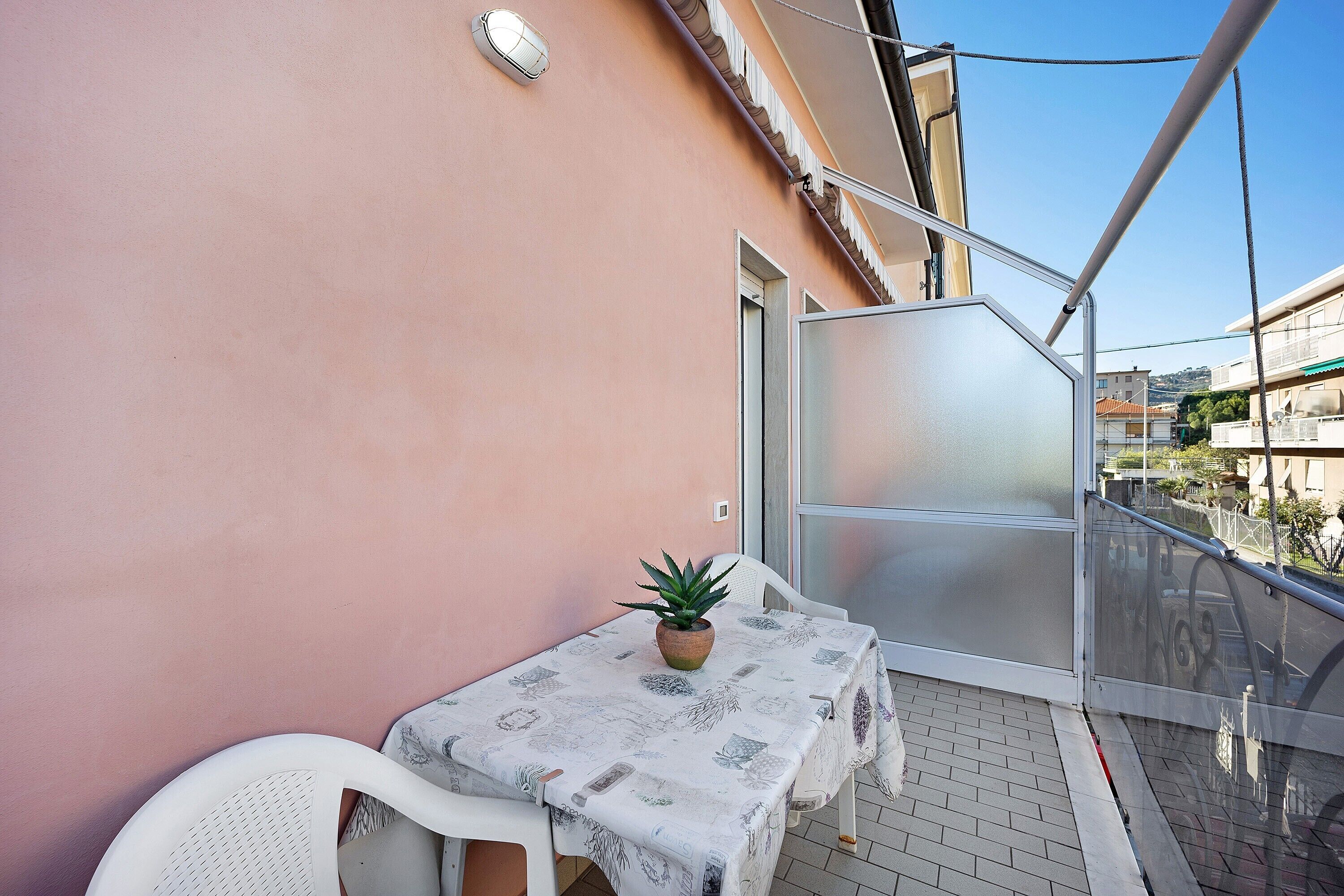 Un balcon avec une table et des chaises, un pot de fleurs et une vue sur les bâtiments.