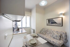A compact living space with a kitchenette, dining area, and a sofa with a framed picture on the wall.