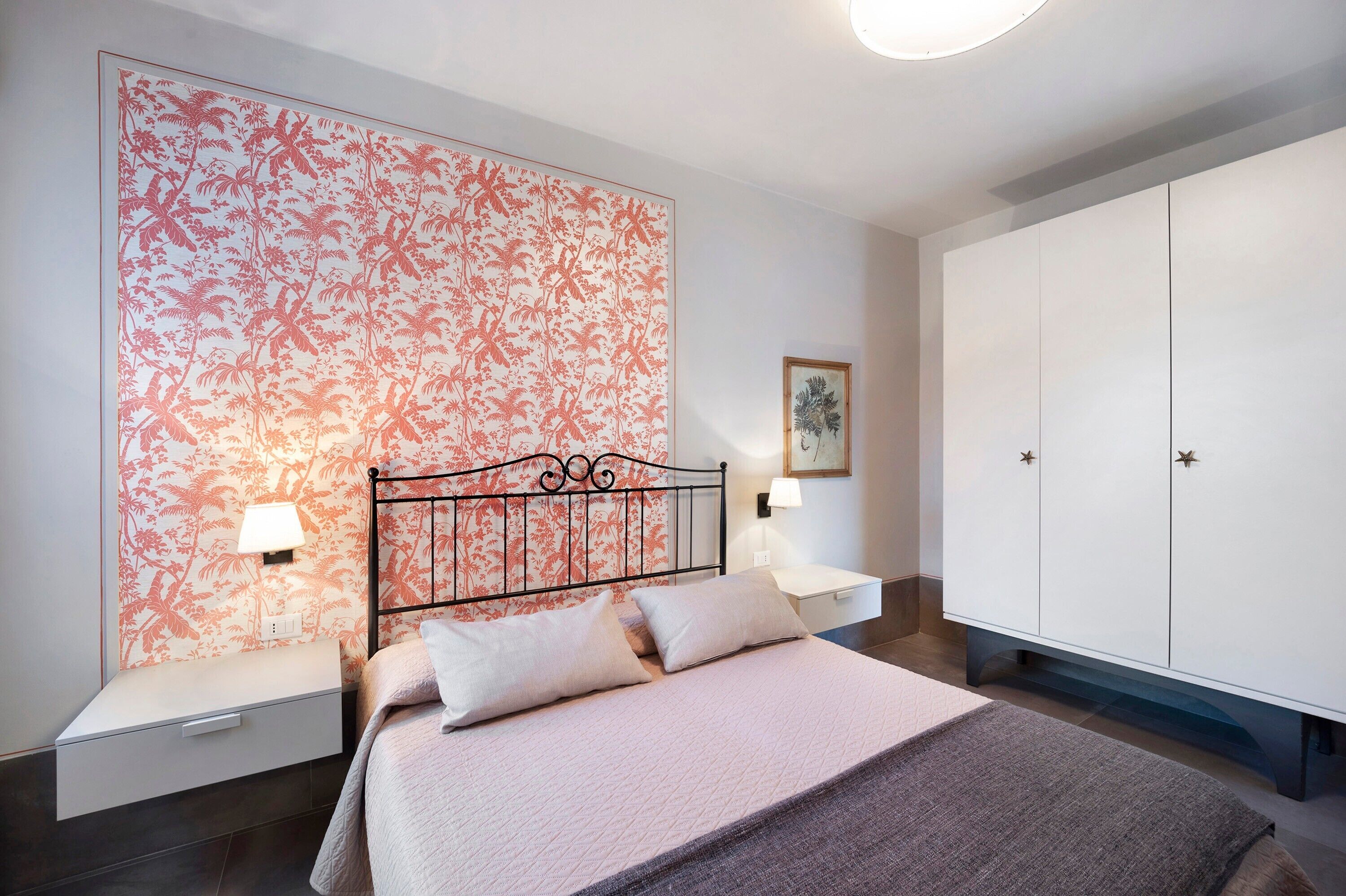 Une chambre à coucher avec un lit, des tables de chevet, une armoire et un papier peint à motifs floraux.