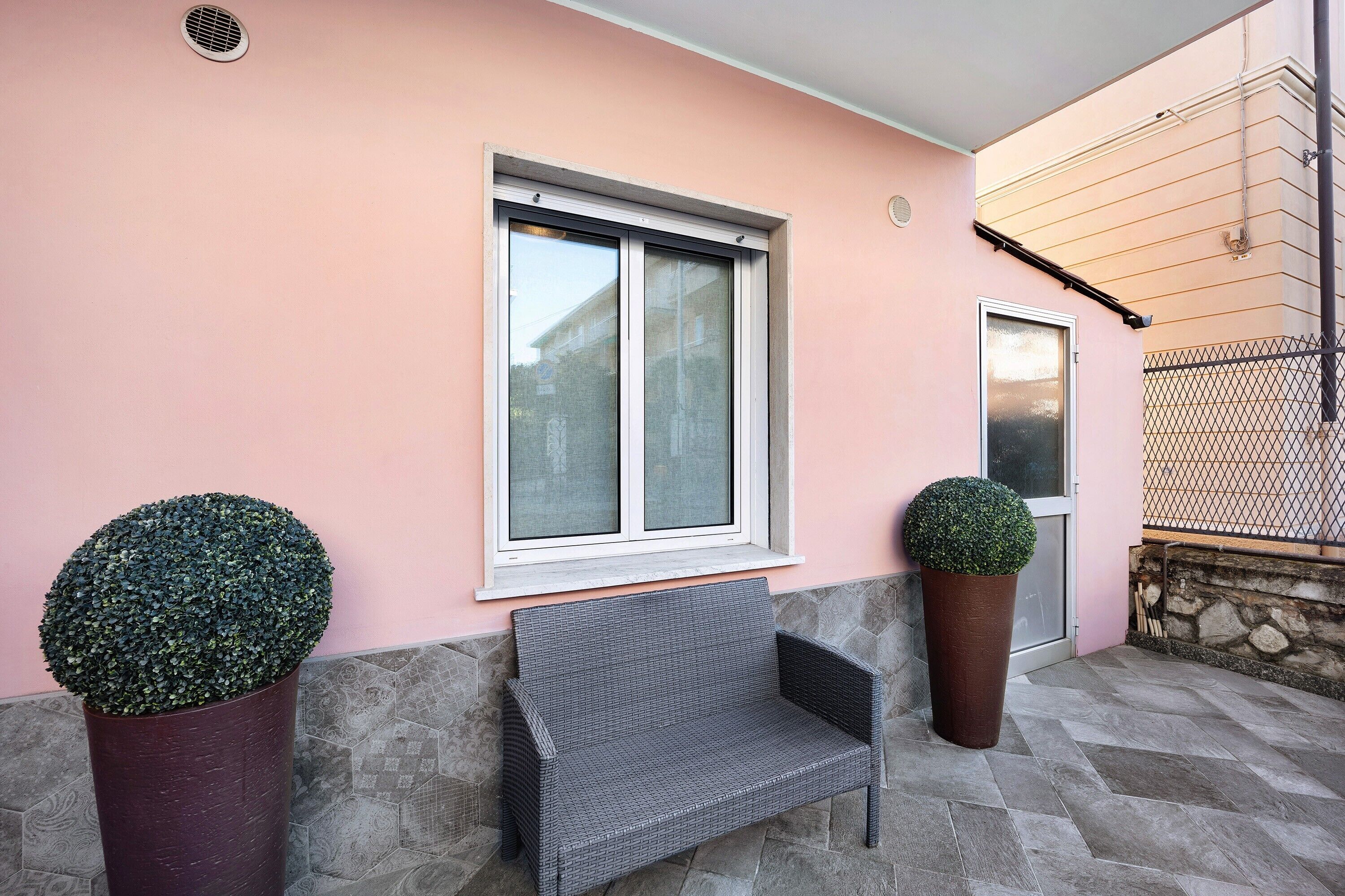 Un banc, deux plantes en pot, une fenêtre et un mur de pierre.