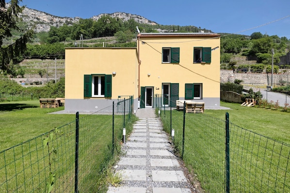 A two-story building with a paved pathway leading to the entrance, surrounded by a green fence.