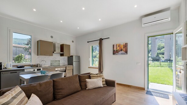 A modern living room with a sofa, a dining table, and a kitchen area. - Ca di perti Apartment 1 with Wi-Fi, A/C & Garden (Finale Ligure)
