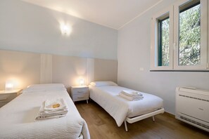 A bedroom with two beds, bedside tables, a window, and an air conditioning unit.