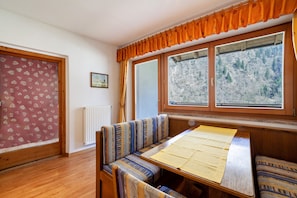 A room with a wooden bench, a table with a yellow tablecloth, and a window with a view of a snowy landscape.