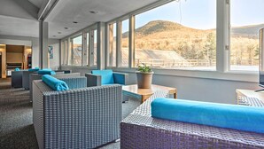 Eine moderne Hotelhalle mit Korbmöbeln, großen Fenstern und Blick auf einen Berg.