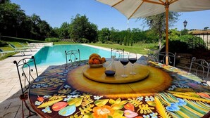 A poolside dining area with a table set for two, surrounded by a pool and greenery. - Tuscan Family Villa with Sauna (Bucine)