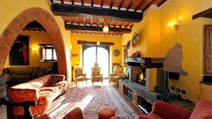 A cozy living room with a fireplace, comfortable seating, and a large window. - Tuscan Family Villa with Sauna (Bucine)