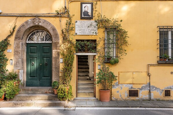 Un edificio amarillo con puerta verde, una escalera y una placa con texto.