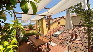 A patio with a wooden table and chairs, potted plants, and a tiled roof.