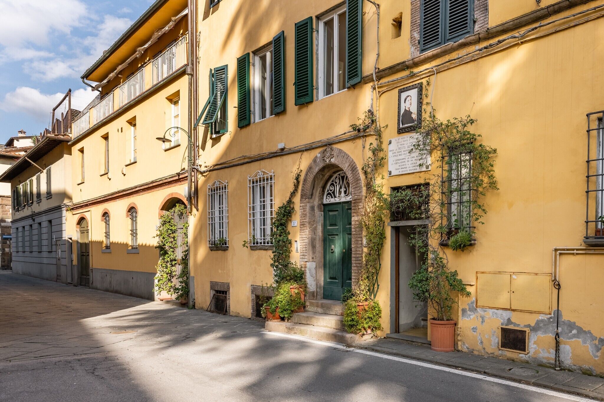 A yellow building with green shutters, a green door, and potted plants.