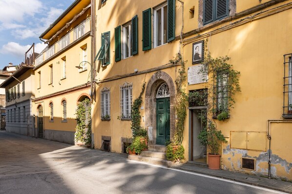 A yellow building with green shutters, a green door, and potted plants.