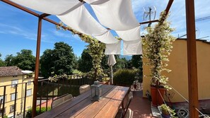 Un patio al aire libre con una mesa de madera, cortinas blancas y plantas trepadoras.