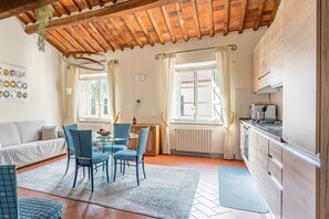 A cozy living room with a sofa, dining table, chairs, and a kitchen area with cabinets and a stove.