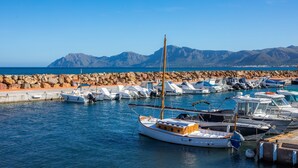 Un port de plaisance avec des bateaux amarrés, une digue rocheuse et des montagnes en arrière-plan.