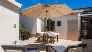 Une terrasse avec une table et des chaises, un grand parasol et des fauteuils de jardin.