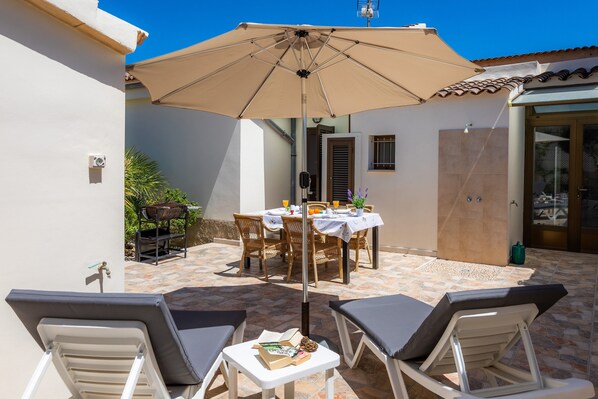 A patio with a table and chairs, a large umbrella, and lounge chairs.