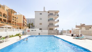 Piscina com superfície de água azul cristalina, rodeada por uma área de lazer branca com espreguiçadeiras.