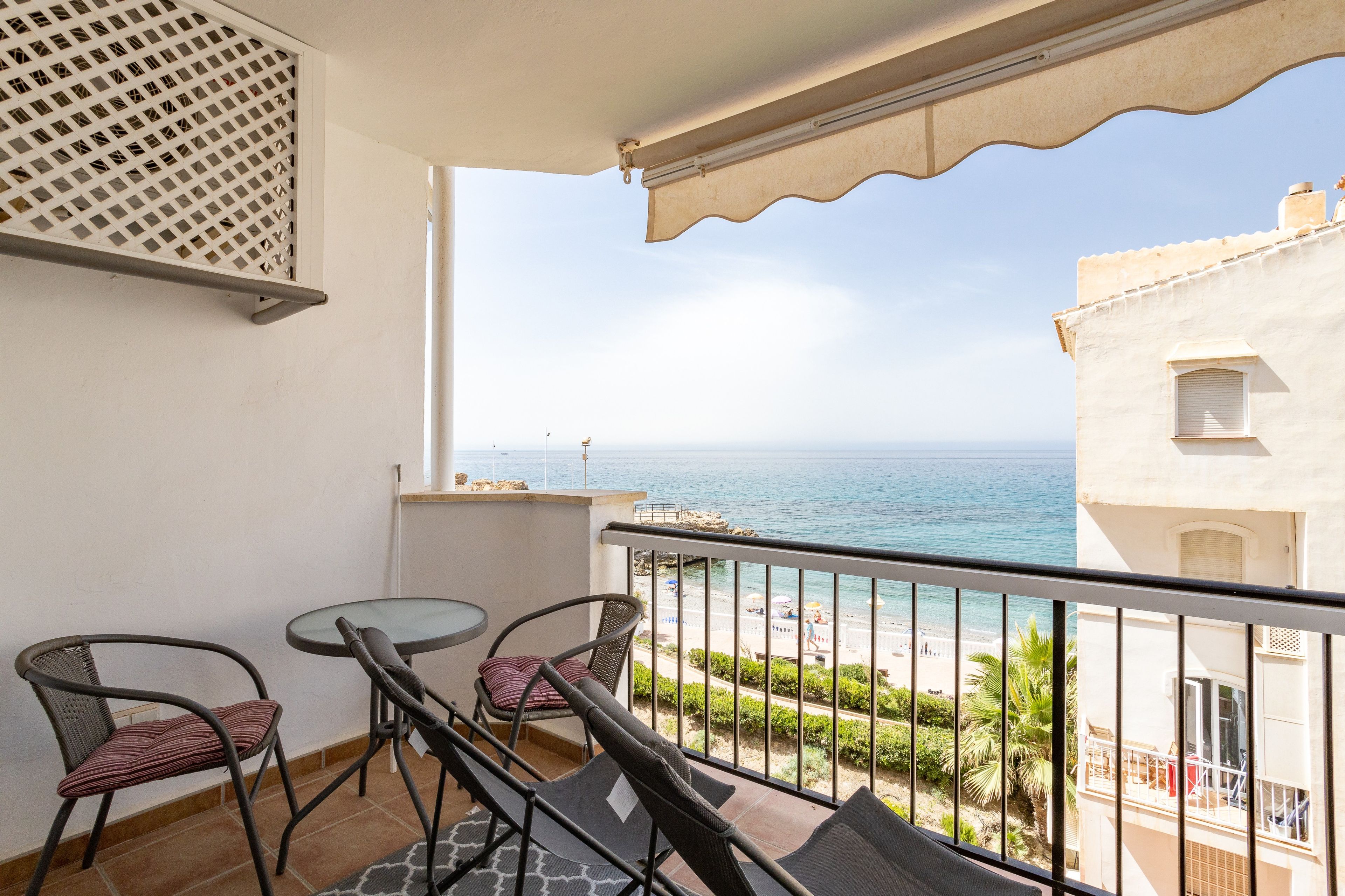 Een balkon met een tafel en stoelen, met uitzicht op een strand en de zee.