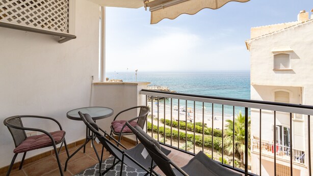 Varanda com mesa e cadeiras, vista para uma praia e o mar.