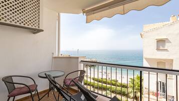 Een balkon met een tafel en stoelen, met uitzicht op een strand en de zee.