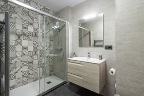 Een moderne badkamer met een douche, wastafel en spiegel.