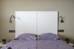 Een slaapkamer met een groot bed, twee bedlampen, een wandcontactdoos en een kleine plant in pot.