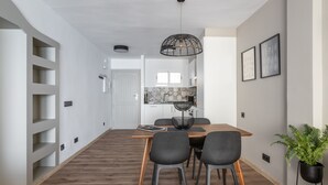 Uma área de refeições moderna com mesa de madeira, quatro cadeiras, luminária pendente e um vaso com planta.