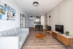 A modern living room with a sofa, a coffee table, a TV, and a dining area with chairs and a table.