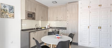 A modern kitchen with wooden cabinets, a microwave, a sink, and a dining area with a table and chairs.