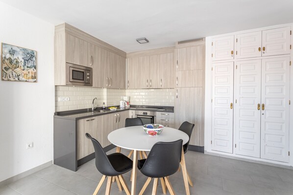 Una cocina moderna con armarios de madera, microondas, lavabo y un comedor con mesa y sillas.