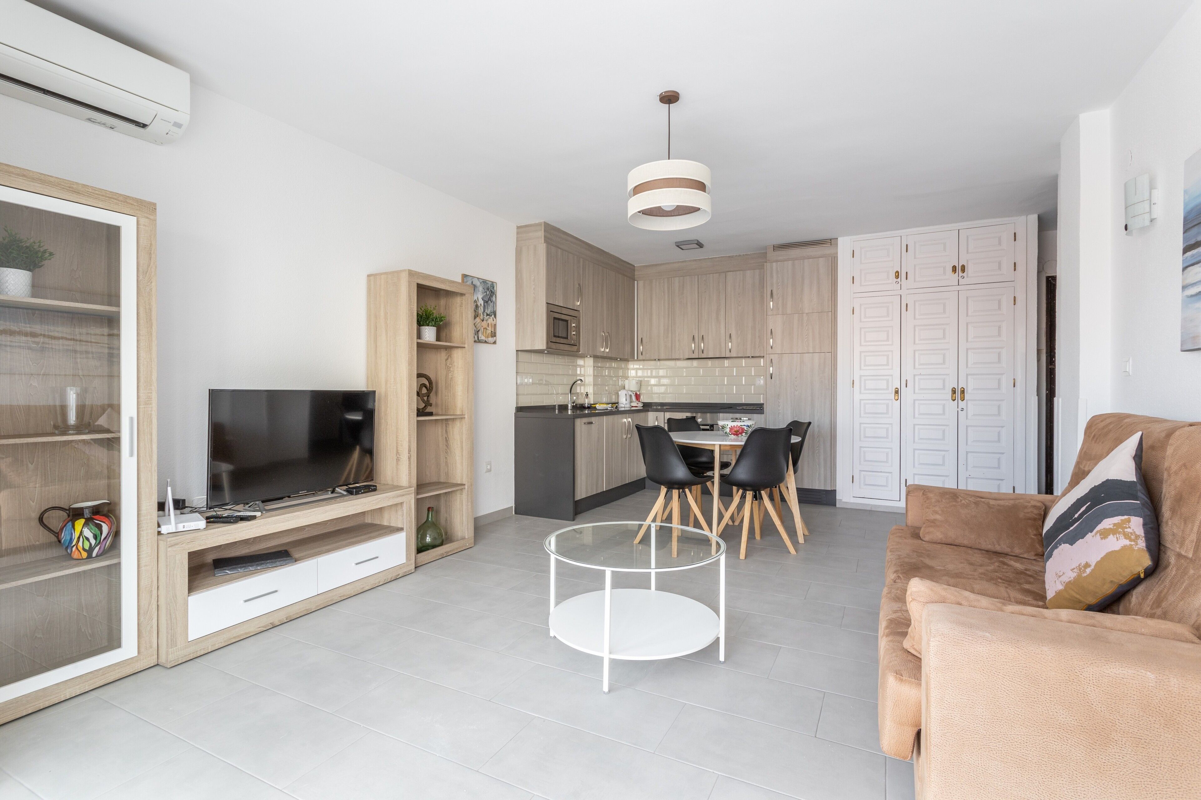 Een moderne woonkamer met een flatscreen televisie, een glazen salontafel en een bruine bank.