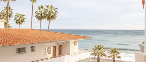 A beachfront property with a tiled roof, multiple windows, and a balcony overlooking the sea.