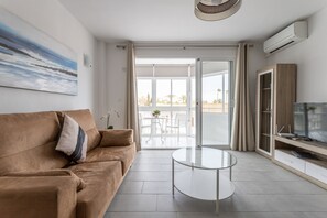 Un salón moderno con un sofá marrón, una mesa de centro de cristal y un televisor de pantalla plana sobre un mueble de madera.