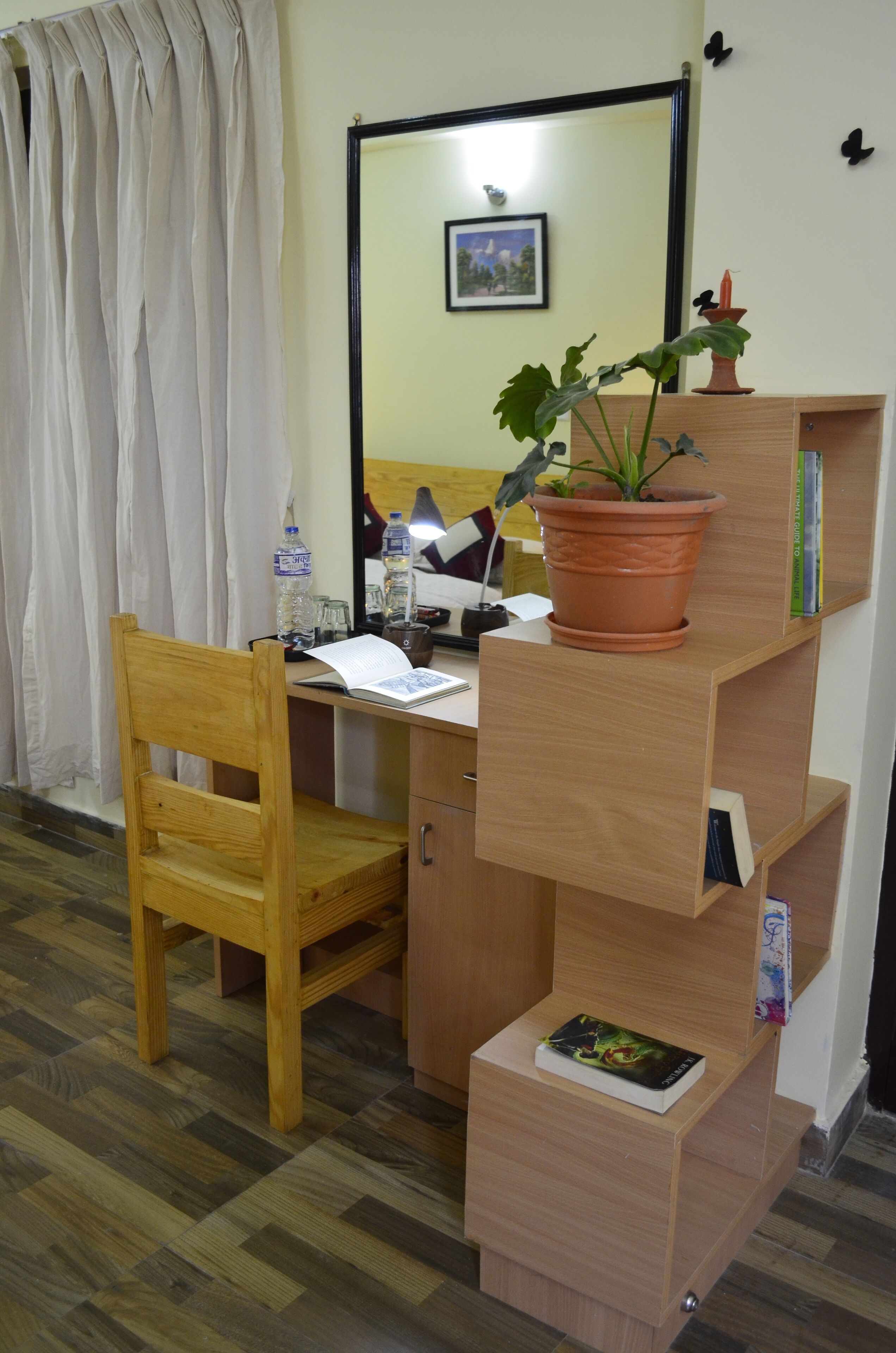 A wooden desk with a chair, a potted plant, a water bottle, and a lamp.