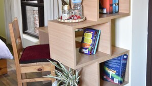 A room with a wooden chair, a small table, a bookshelf, and a potted plant. - Tanani Newa Home (FishTail) (Lalitpur)