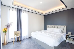 Una habitación de hotel moderna con una cama grande, una mesita de noche, un florero con flores y vistas al exterior a través de la ventana.
