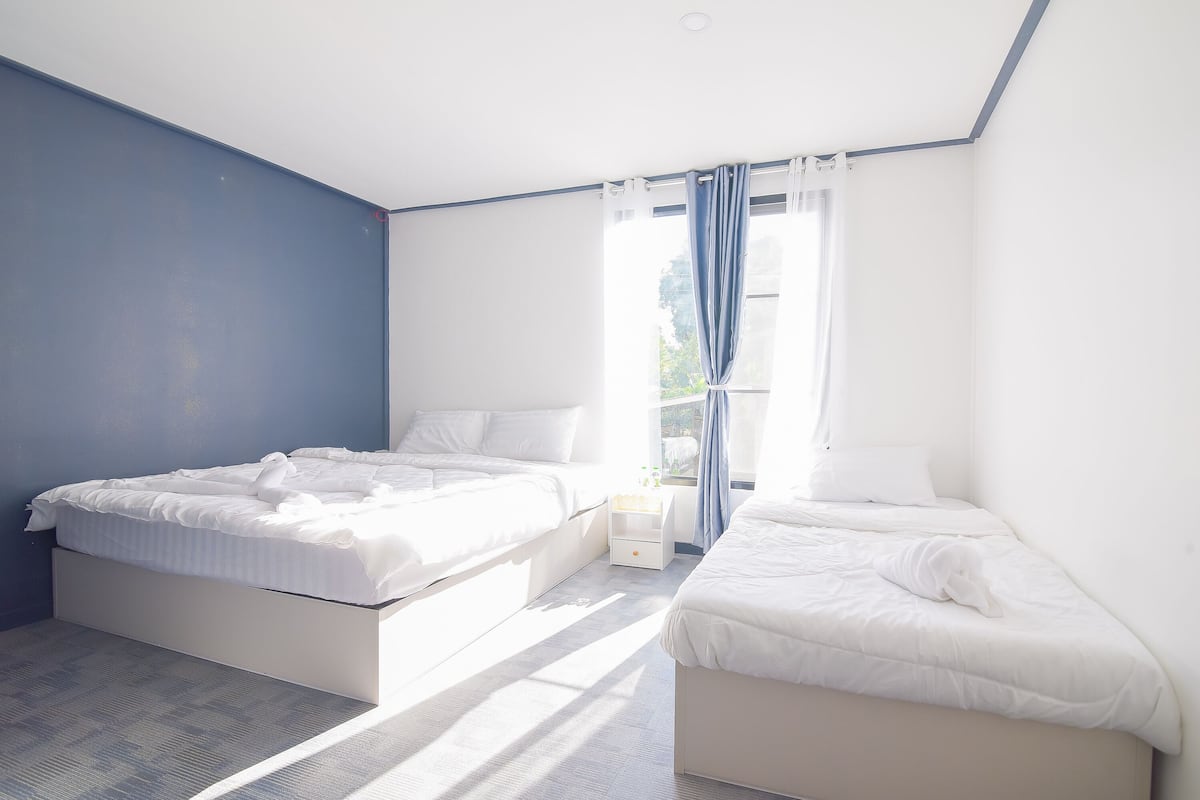 A bedroom with two beds, a window with curtains, and a small bedside table.
