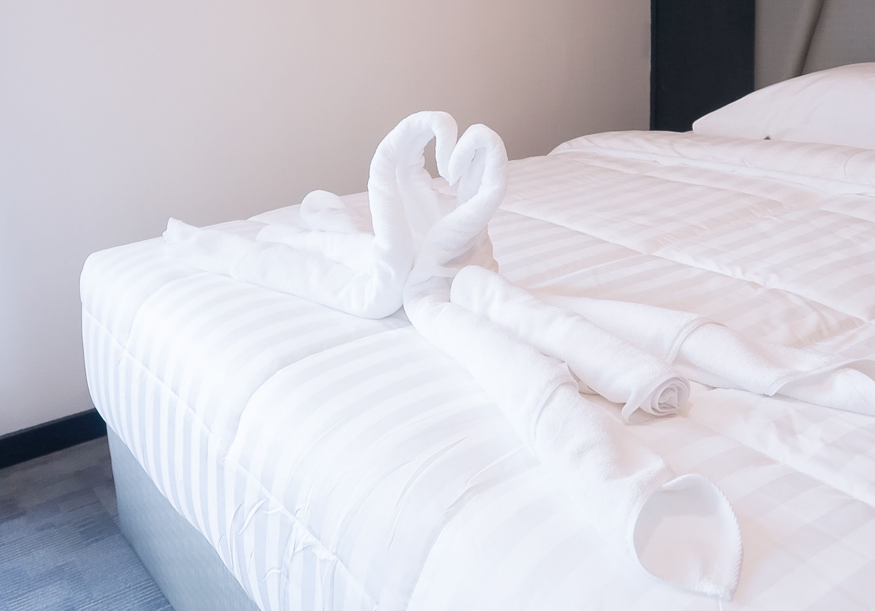 A neatly made bed with white linens and a heart-shaped towel arrangement.