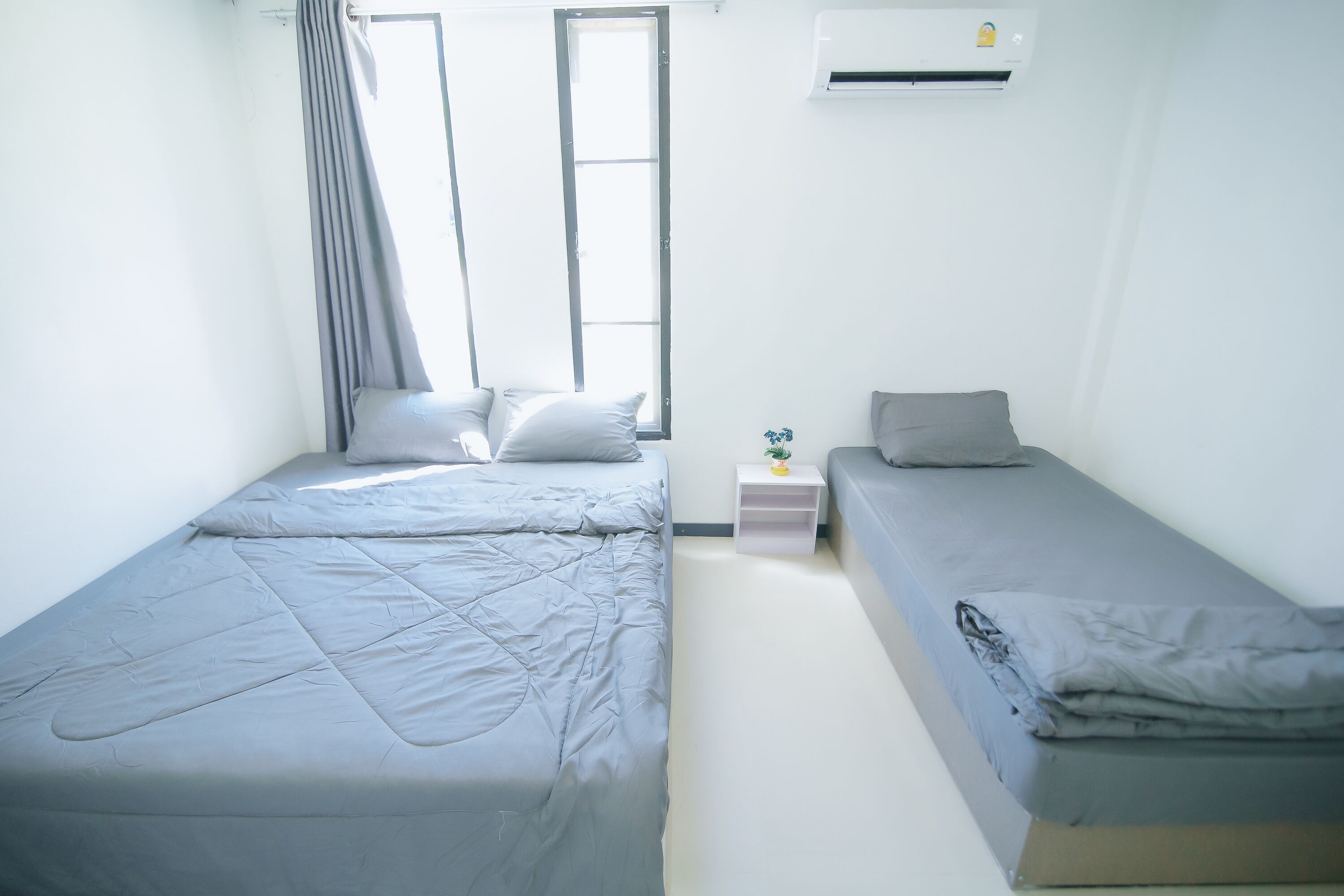 A room with two single beds, a small bedside table with a lamp, and a window with curtains.
