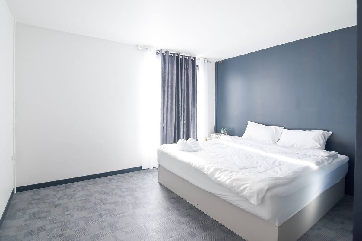 A modern bedroom with a large bed, a dark accent wall, and a grey patterned floor.