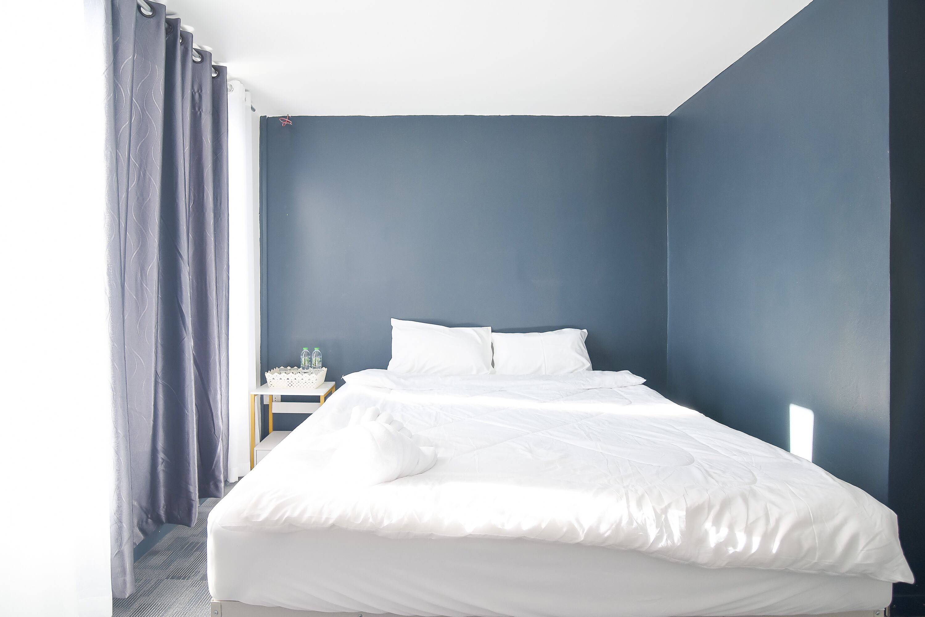 Un lit bien fait, avec du linge de lit blanc, dans une pièce aux murs bleu foncé et au plafond blanc.