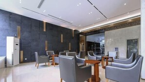 Un hall d’entrée moderne avec des fauteuils en cuir gris, des tables en bois et un grand miroir.
