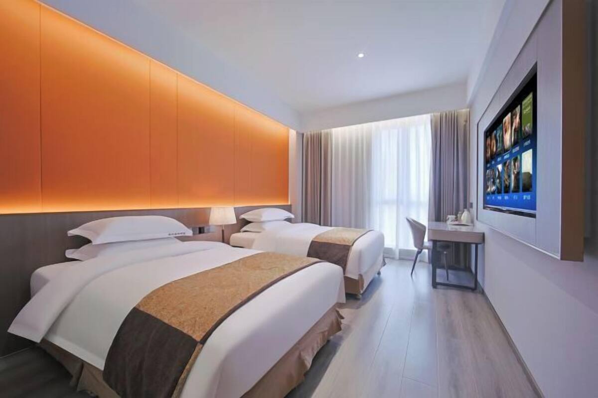 A hotel room with two beds, a desk, and a TV mounted on the wall.