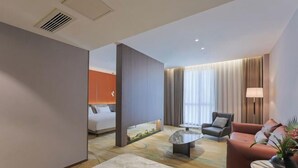 Een moderne hotelkamer met een bed, een zithoek met een bank en fauteuil, een salontafel en een groot raam met gordijnen.