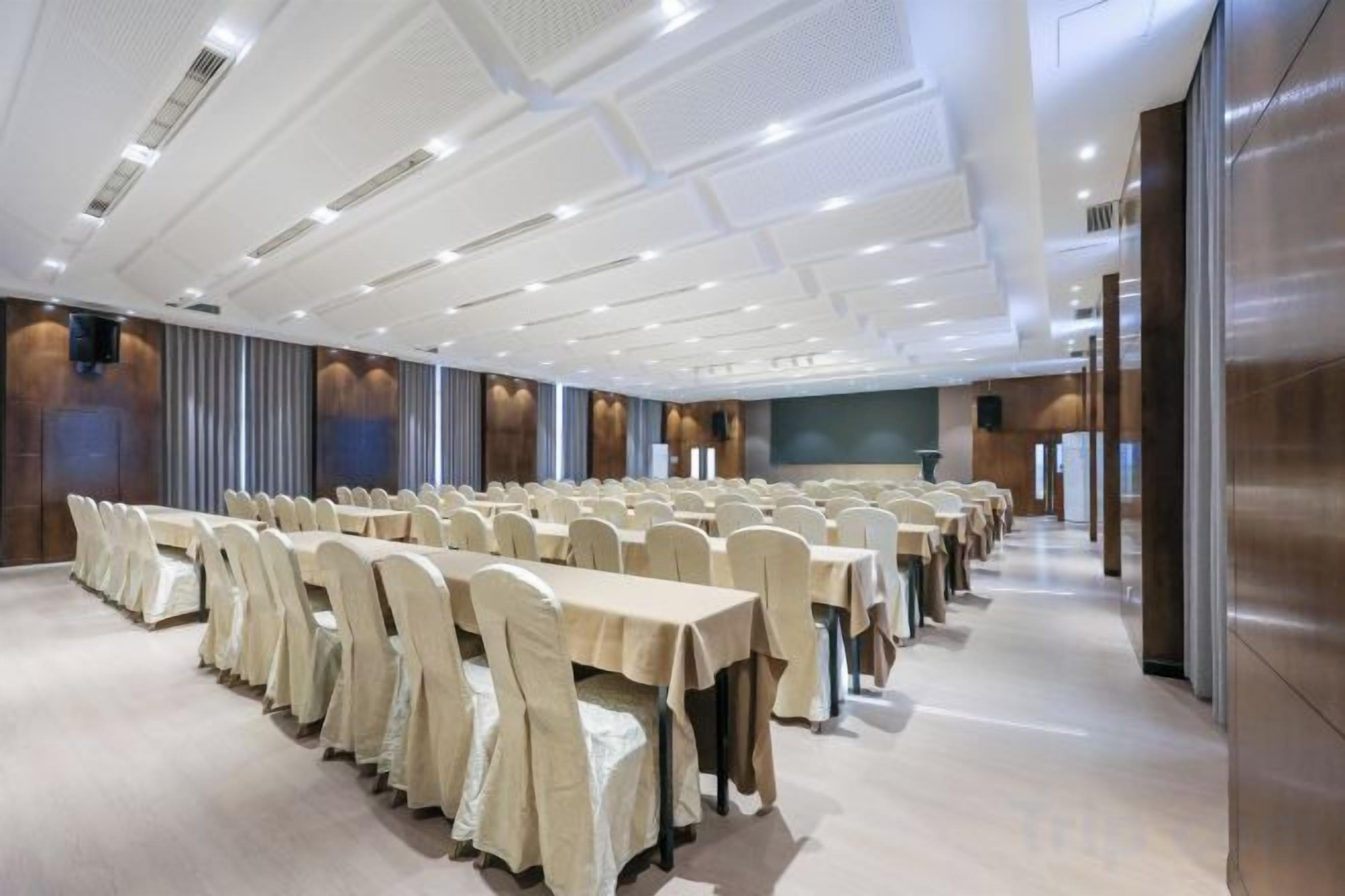 A conference room with rows of tables and chairs, a large screen, and a modern ceiling design.
