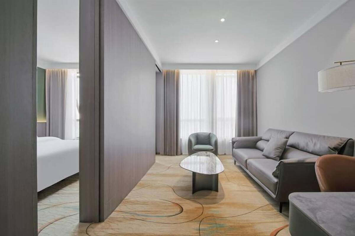 A modern hotel room with a bed, a sofa, a chair, and a coffee table.